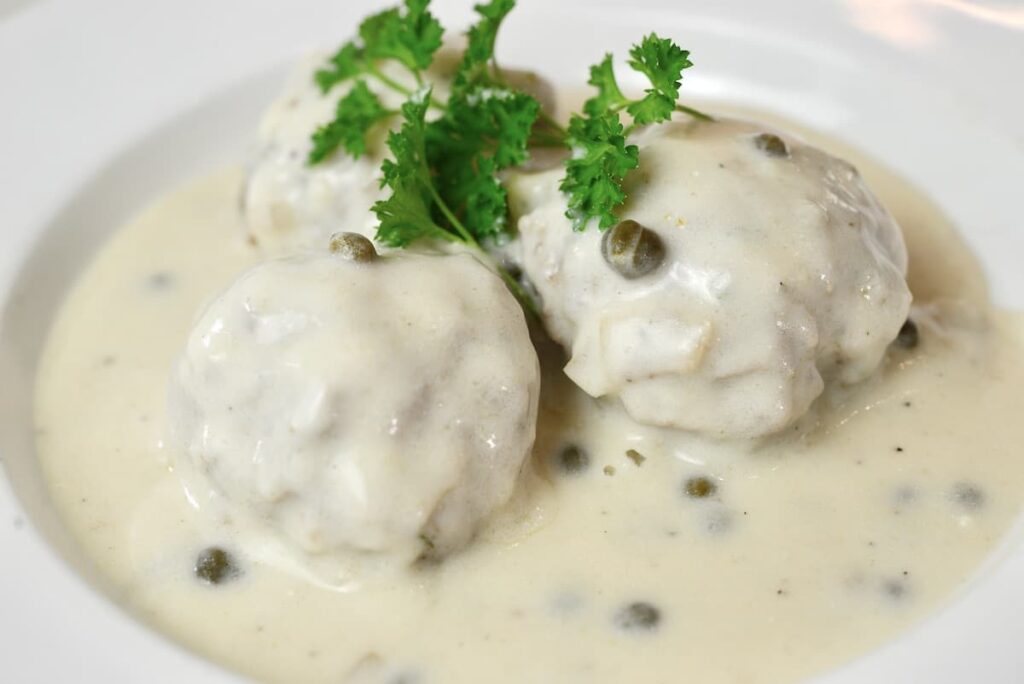 3 German meatballs in white sauce on plate with fresh parsley