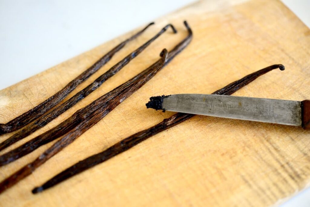 vanilla bean pods on cutting board with knife with vanilla seeds on tip