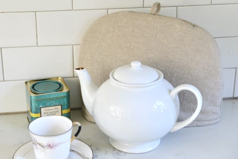 white tea pot with cozy, tin of breakfast tea and cup on saucer