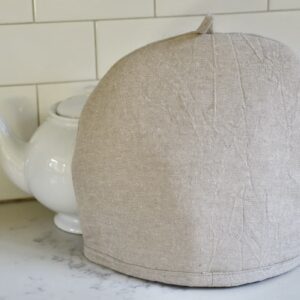 linen tea cozy in front of white tea pot
