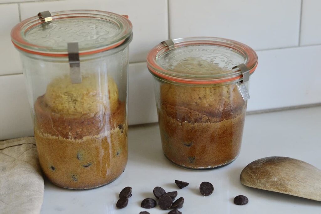 2 cakes in glass jars on kitchen counter with chocolate chips and wooden spoon