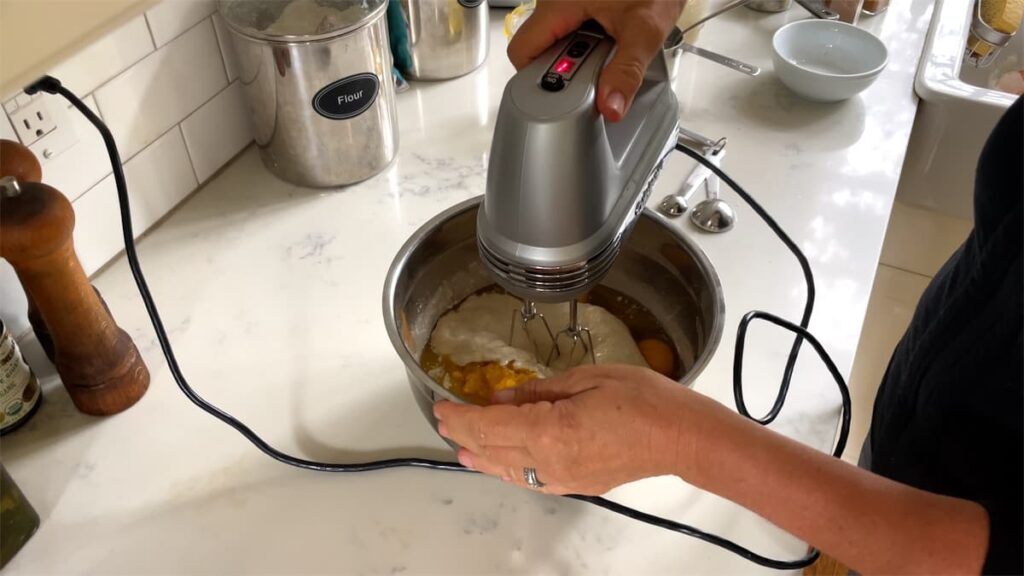 woman holding electric mixer in bowl with dry and wet ingredients