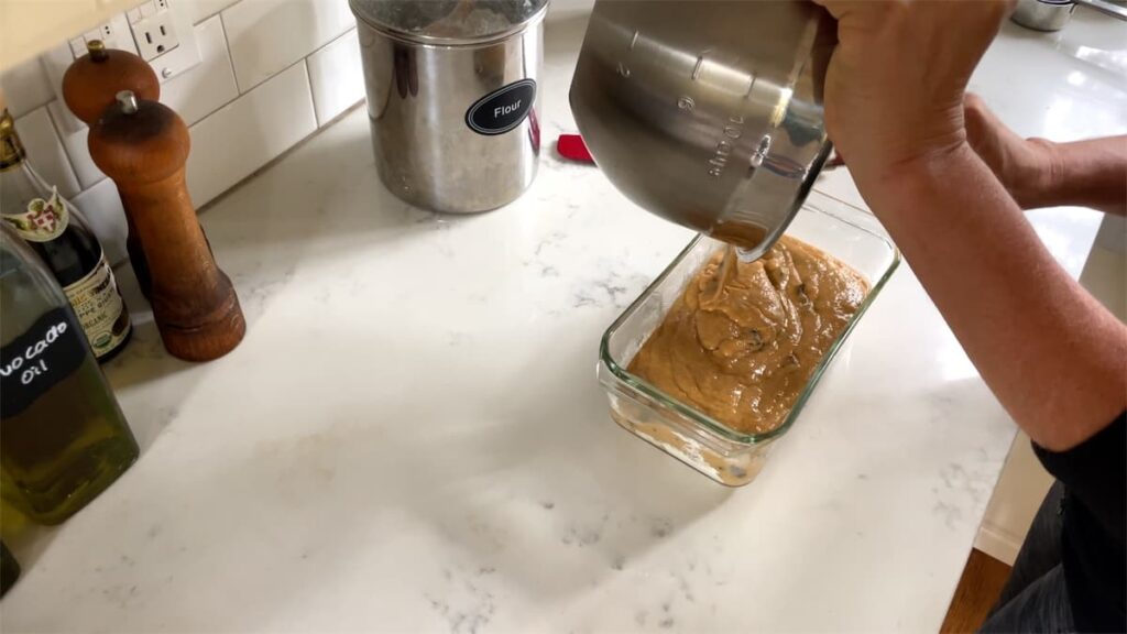 woman pouring sourdough pumpkin dough into glass loaf pan