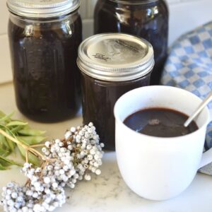 jars and cup with elderberry juice next to elderberries on kitchen counter