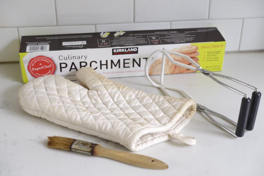 parchment paper, jar lifter, oven mitt, and pastry brush on kitchen counter