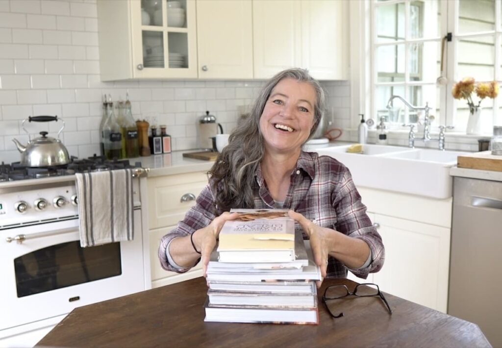 woman with stack of 8 sourdough books on kitchen table