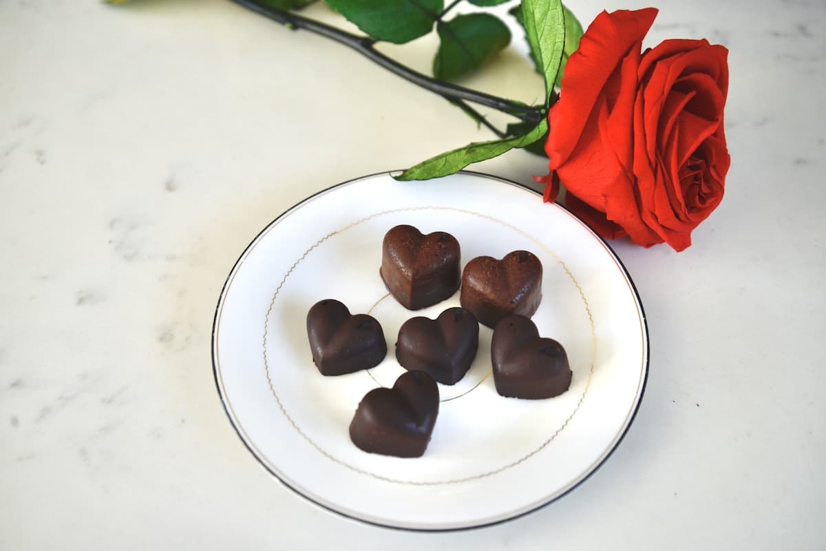 chocolate hearts on white plate next to red rose