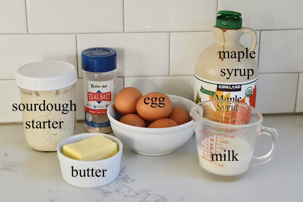 jar of sourdough starter, sea salt, eggs, maple syrup, butter, and milk on kitchen counter