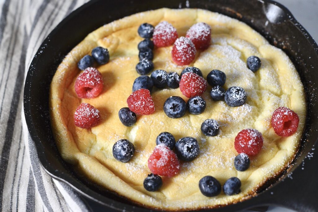 sourdough dutch pancake in cast iron skillet with berries and powdered sugar