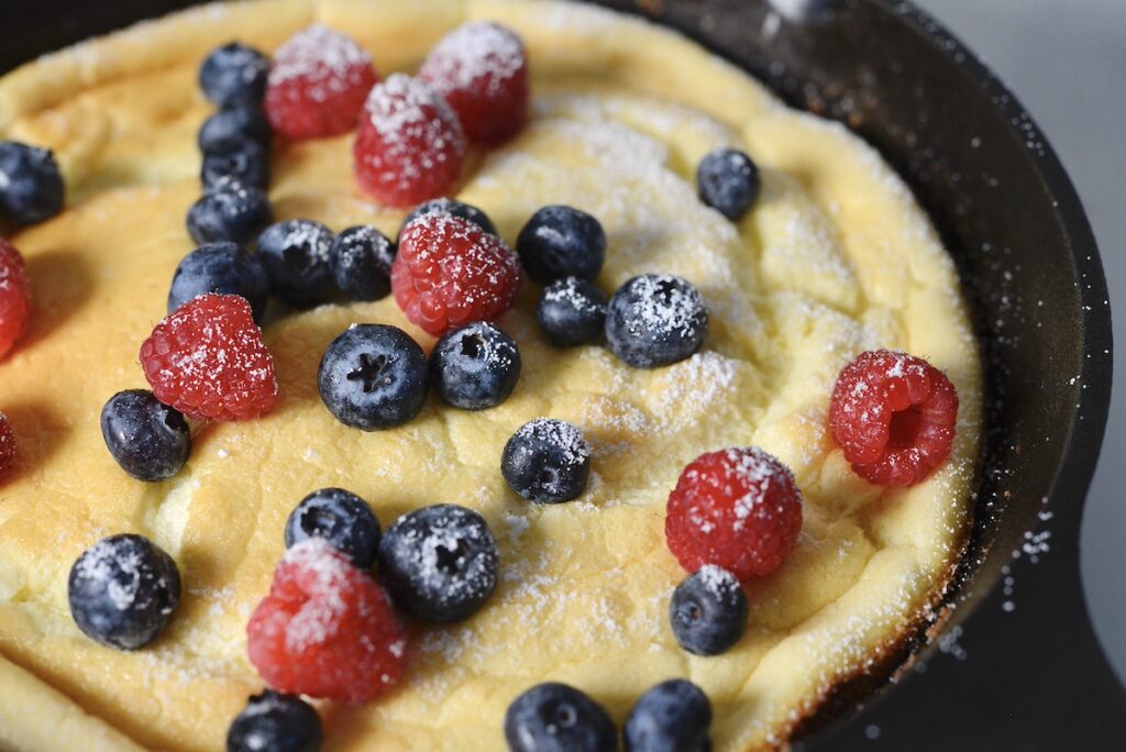 sourdough dutch baby in cast iron skillet with blueberries and raspberries and powdered sugar