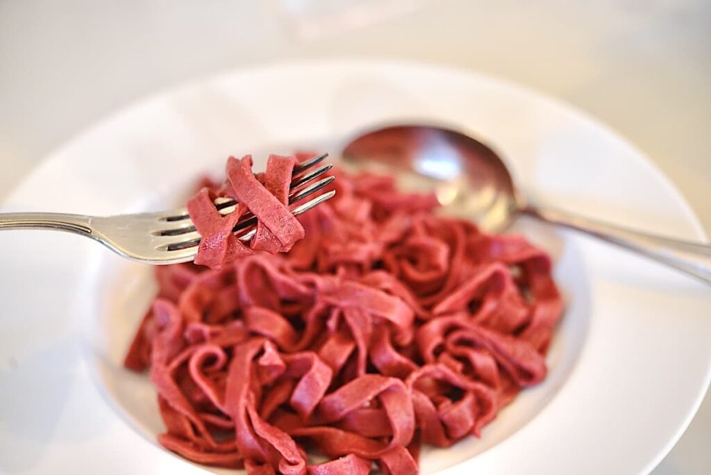 white bowl with red beet pasta on fork