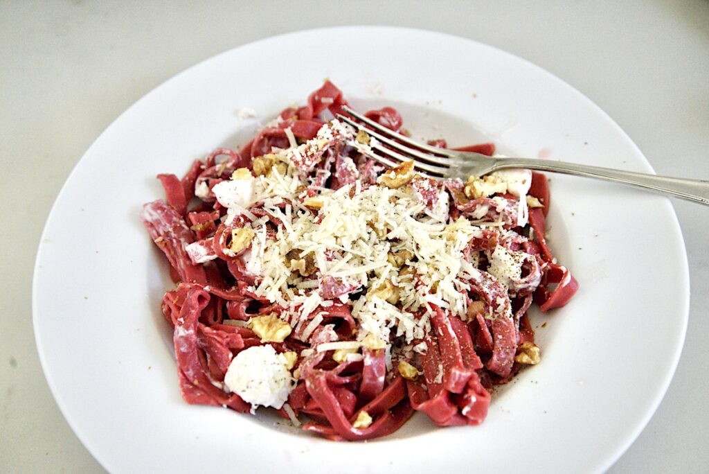 white bowl with red beet pasta with white sauce