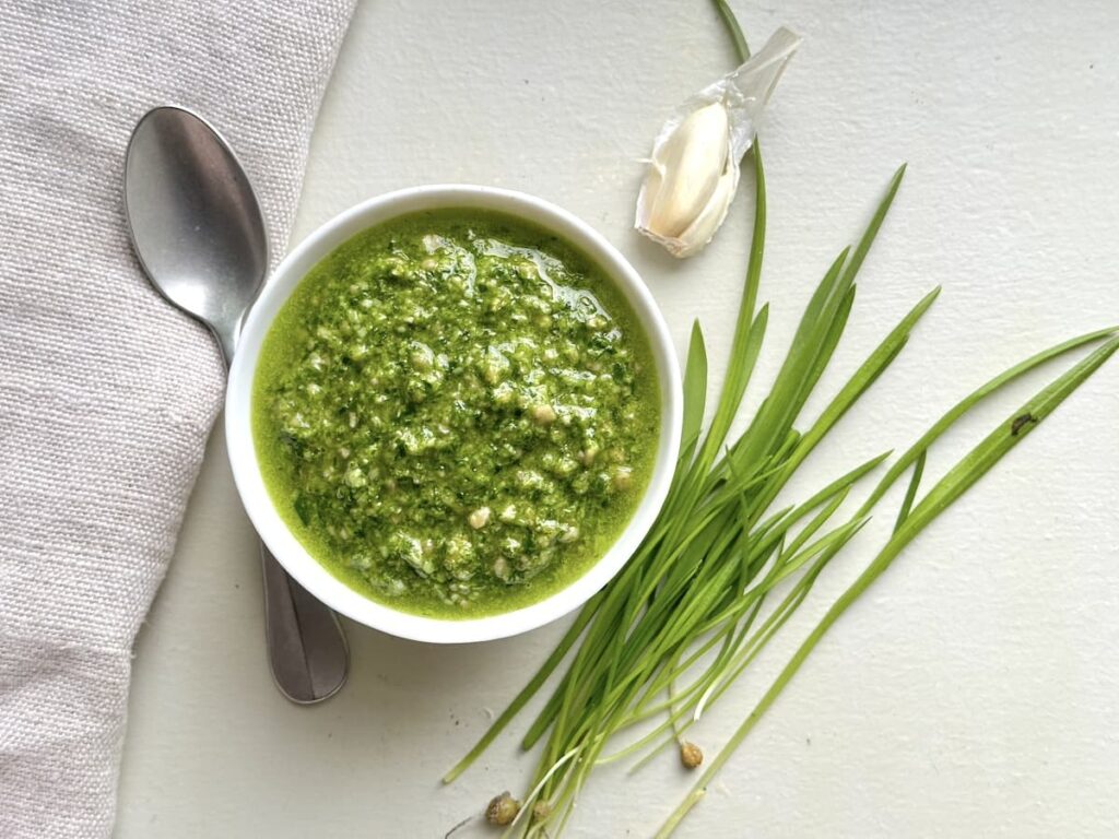 ramp pesto in bowl with spoon, garlic clove, and ramp leaves