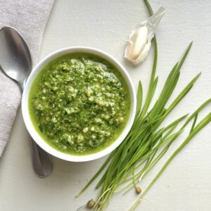 ramp pesto in bowl next to garlic clove, ramp leaves, and spoon