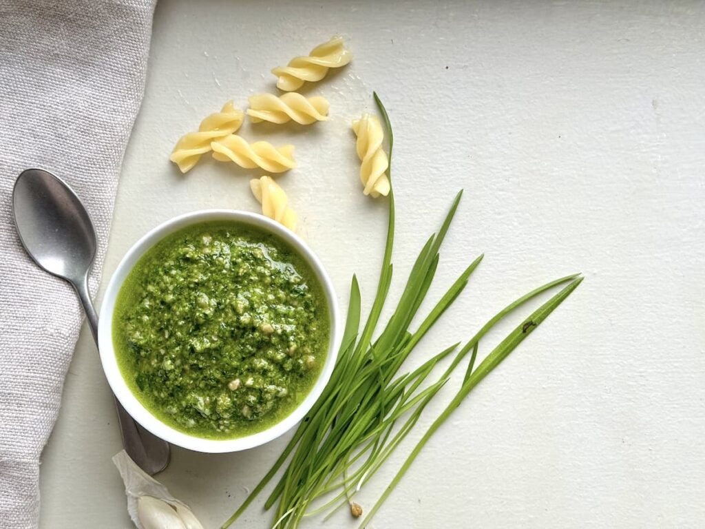 ramp pesto in bowl with spoon, cooked noodles, and ramp leaves