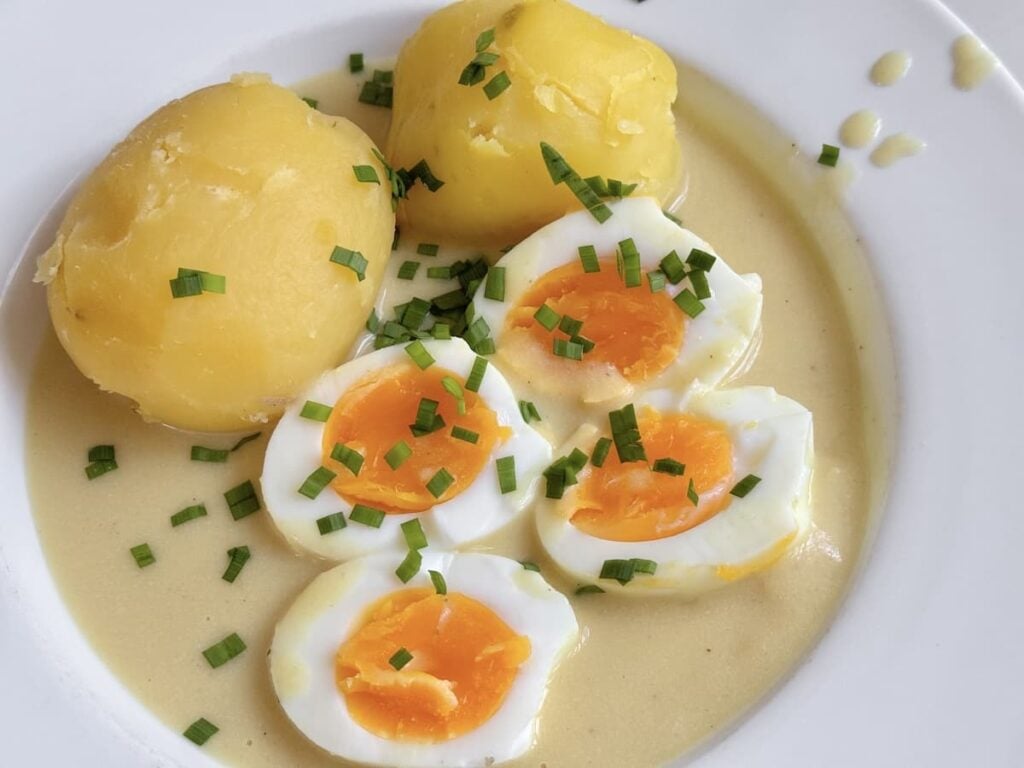 soft boiled egg halves with potatoes in mustard sauce sprinkled with chopped chives