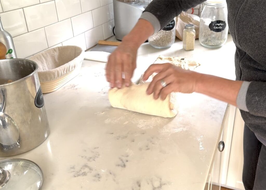 woman rolling stretched out dough into a log