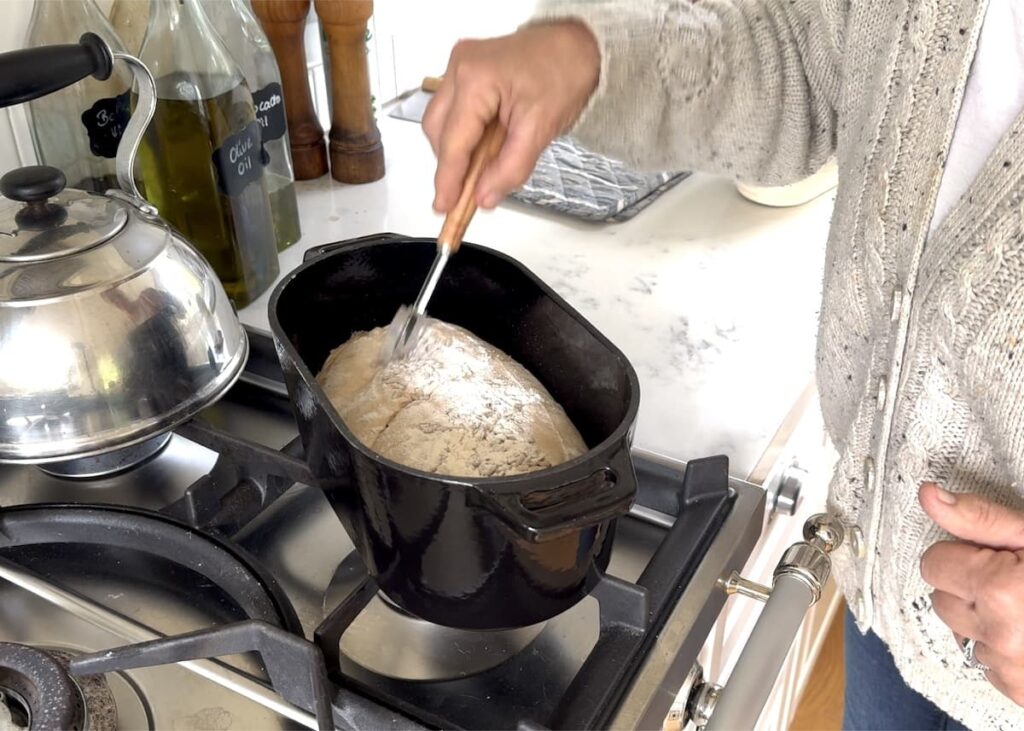 woman scoring top of dough in cast iron Dutch oven with bread lame