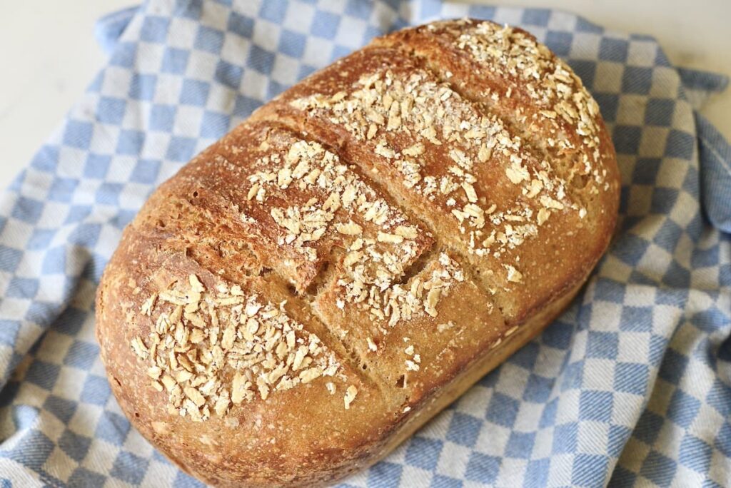 loaf of seeded sourdough sandwich bread on blue kitchen towel