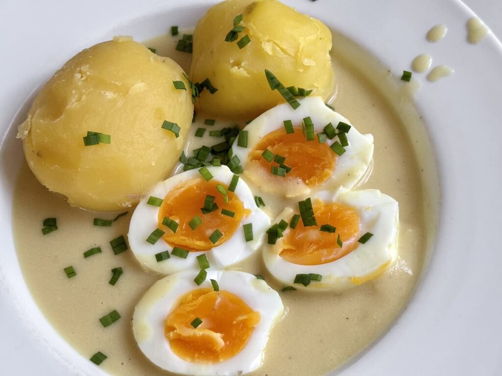 halved, soft-boiled eggs on plate with boiled potatoes, and mustard sauce