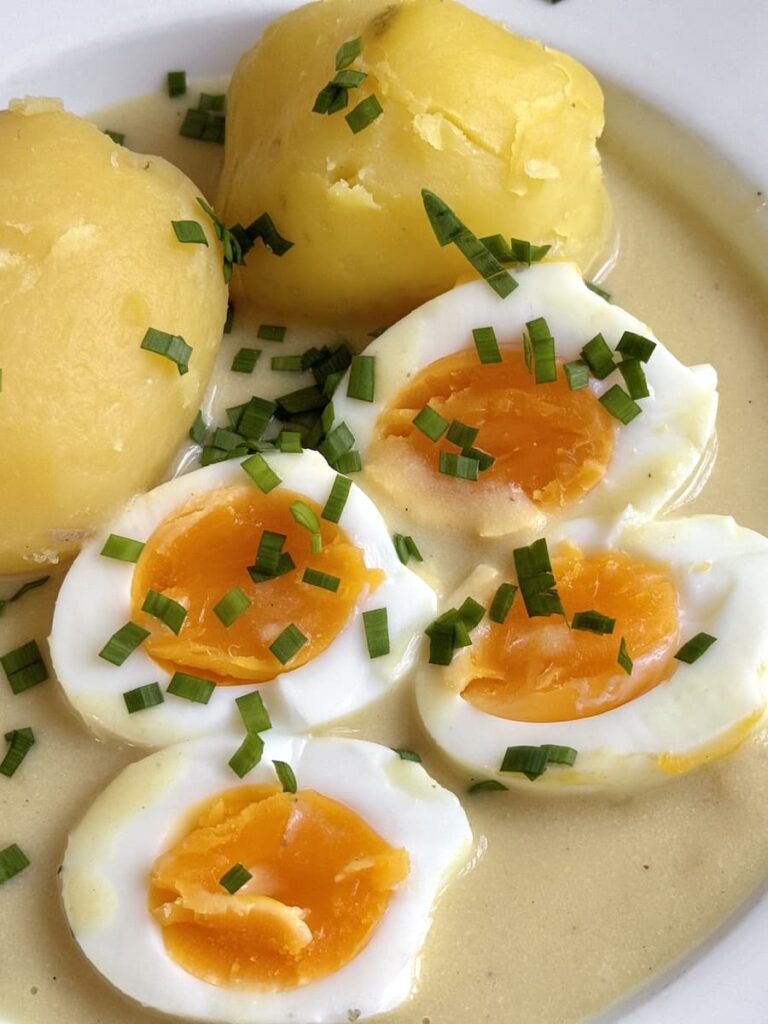 soft boiled eggs cut open on plate with potatoes and mustard sauce