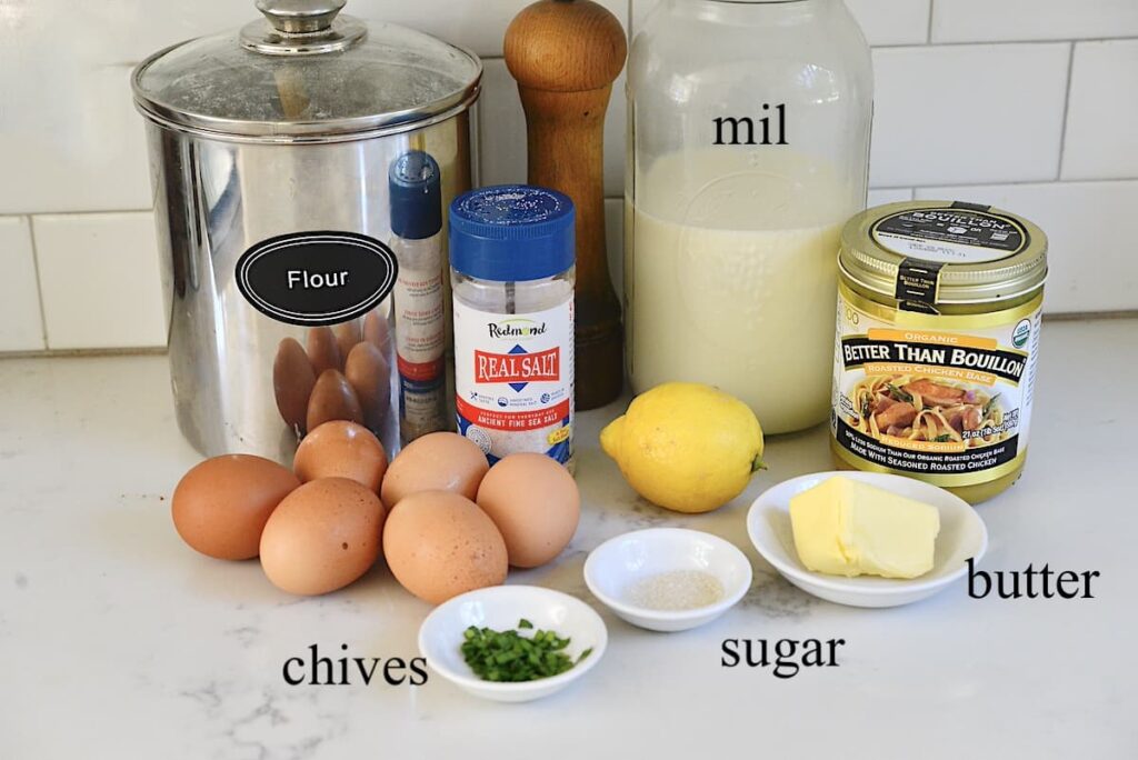 flour, sea salt, pepper mill, milk, chicken bouillon, butter, lemon, sugar, eggs, and chives on kitchen counter