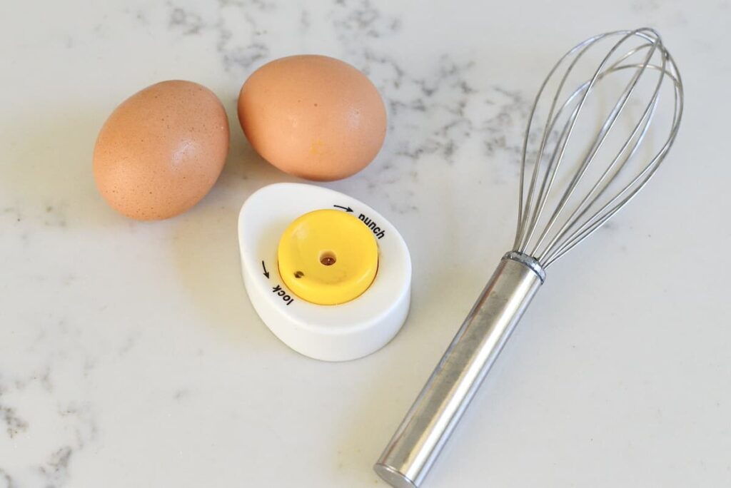 2 eggs, egg punch, wire whisk on kitchen counter