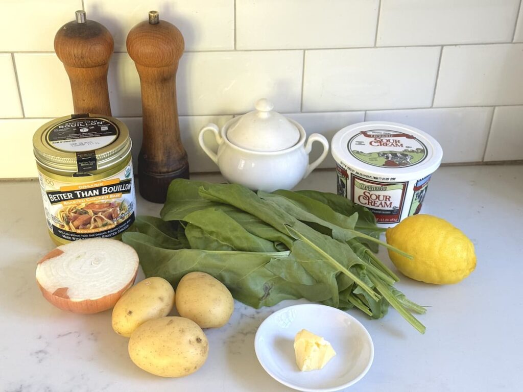 sorrel leaves, potatoes, half an onion, chicken bouillon, sour cream, butter, lemon, salt and pepper on kitchen counter