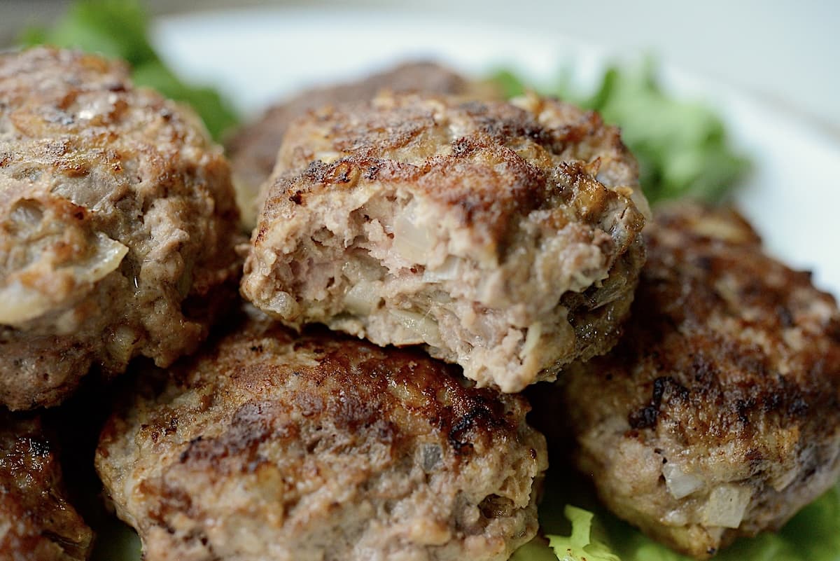 Close up of 4 cooked frikadellen, with a bite taken out of one of the frikadelle.