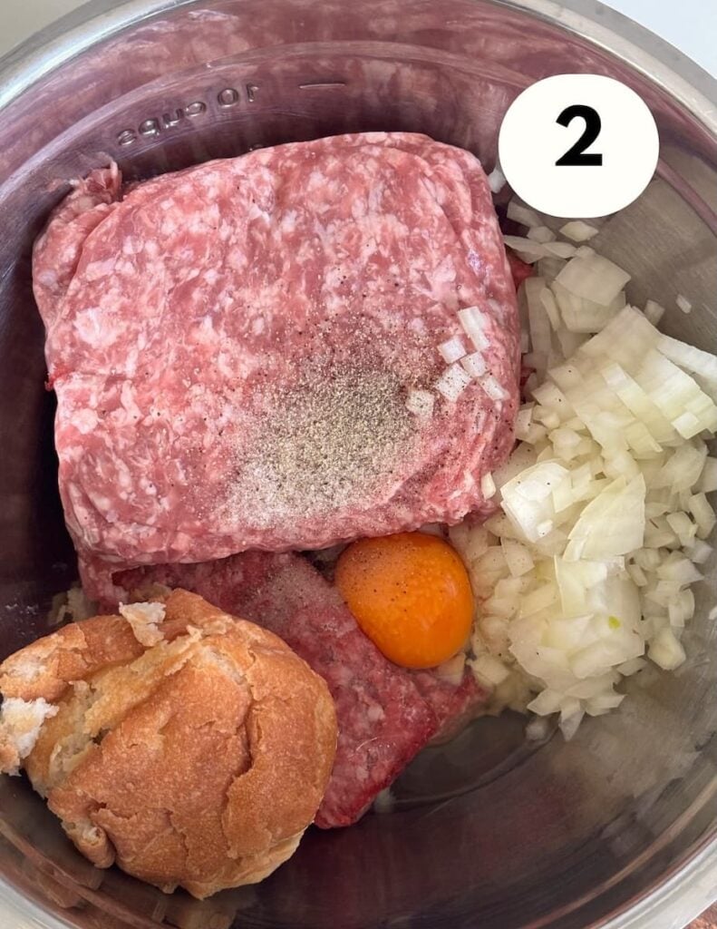 Raw ground beef in a mixing bowl with a raw egg, soaked bread, minced onion and spices.