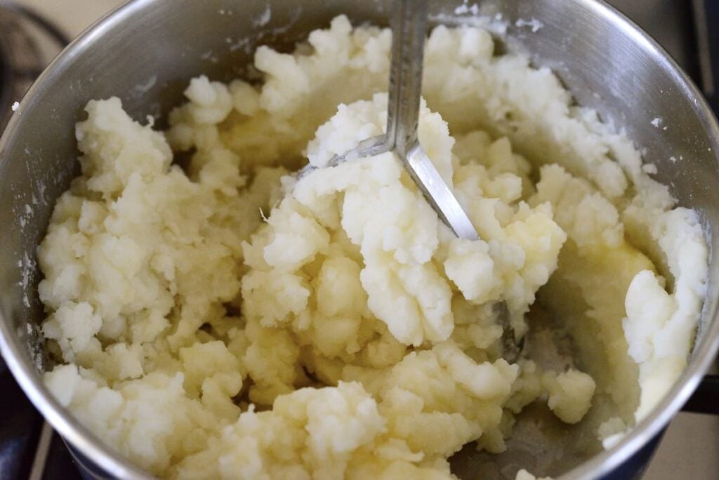 mashed potatoes in pot with potato masher