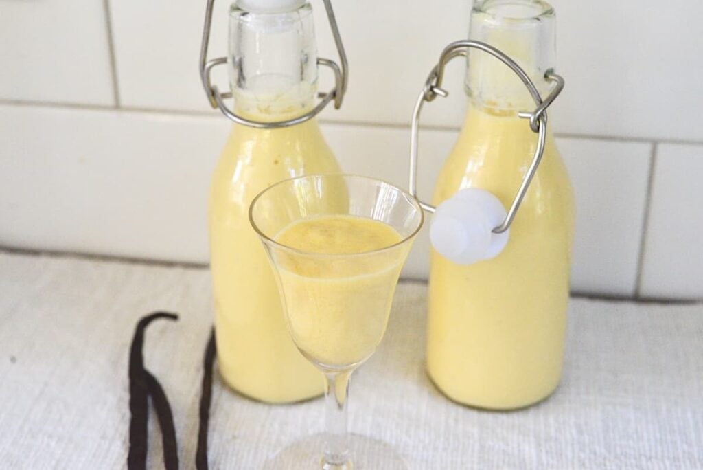 German egg liqueur in 2 small bottles and one tulip glass with vanilla beans on kitchen counter