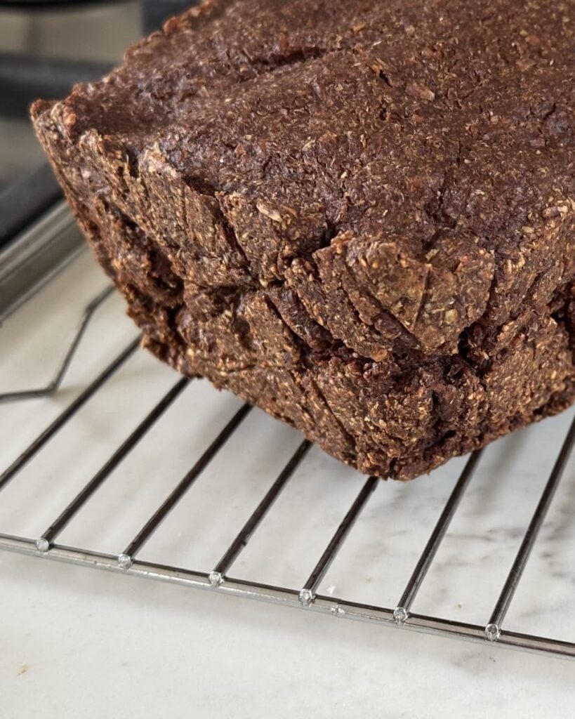 Loaf of freshly baked pumpernickel bread on a wire rack.