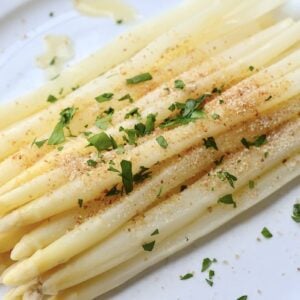 bunch of cooked white asparagus plate with butter, breadcrumbs, and chopped parsley