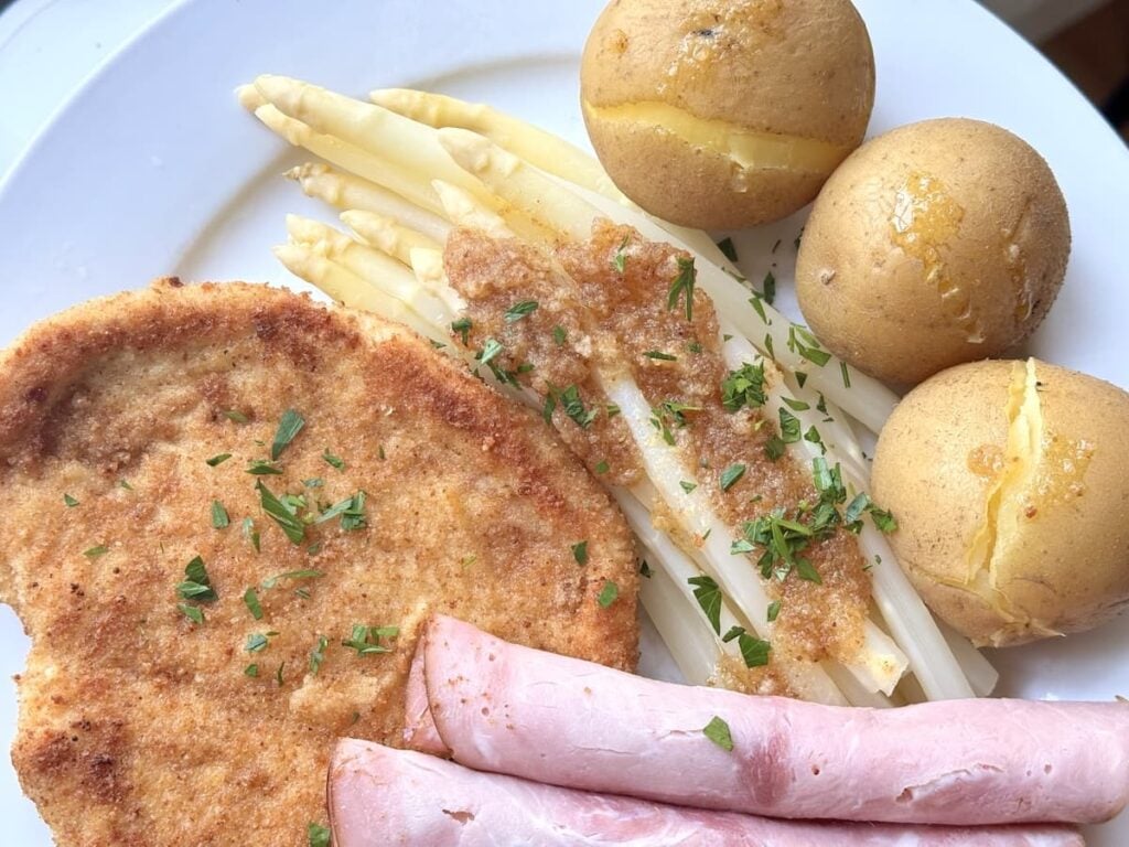 white asparagus on plate with boiled potatoes, ham, and schnitzel