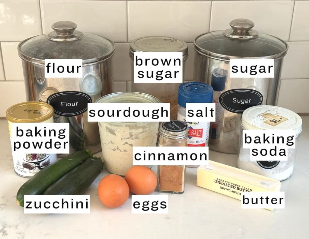 ingredients for sourdough zucchini bread: flour, brown sugar, sugar, baking powder, sourdough, salt, baking soda, butter, cinnamon, eggs, zucchini