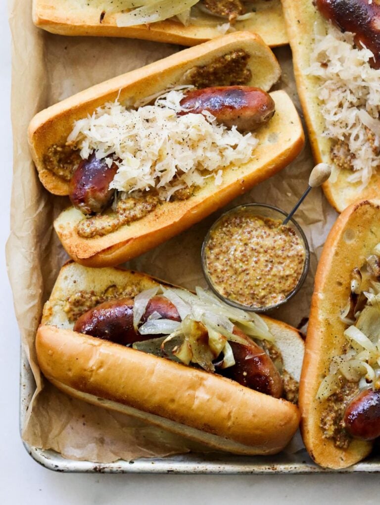 Overhead of baked brats in buns, topped with sauerkraut.