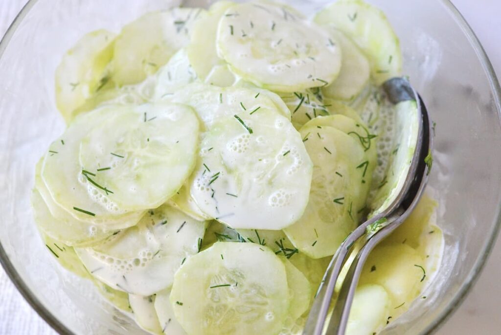 German cucumber salad in glass bowl with salad servers