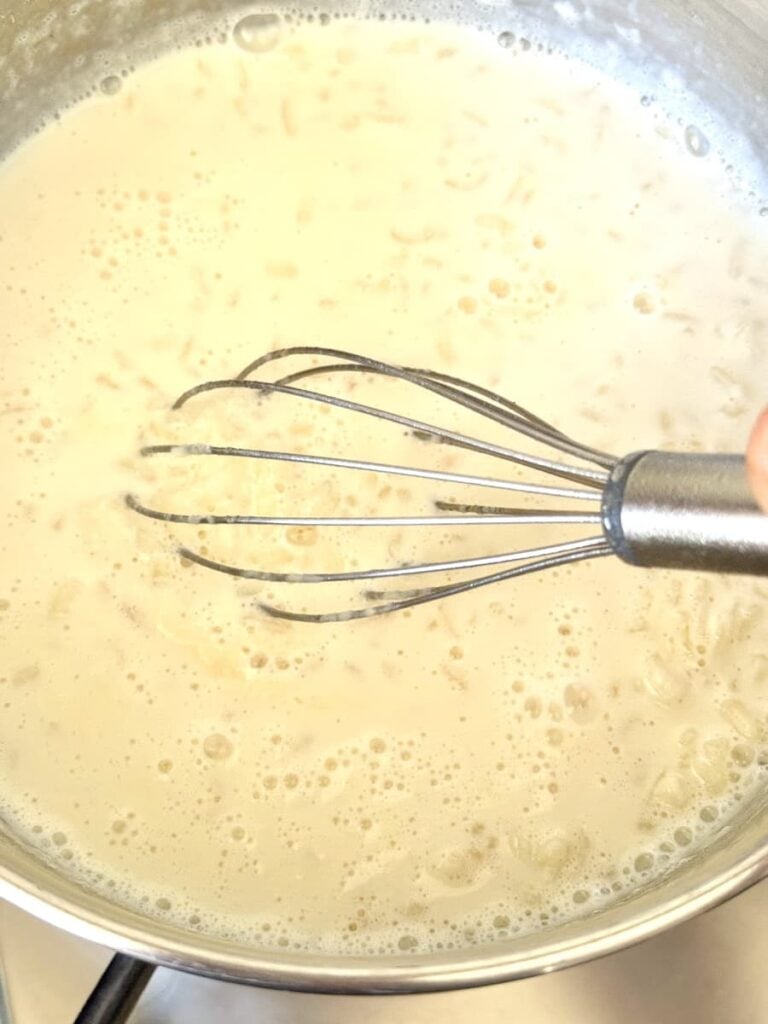 Milchreis in saucepan on stovetop with wire whisk