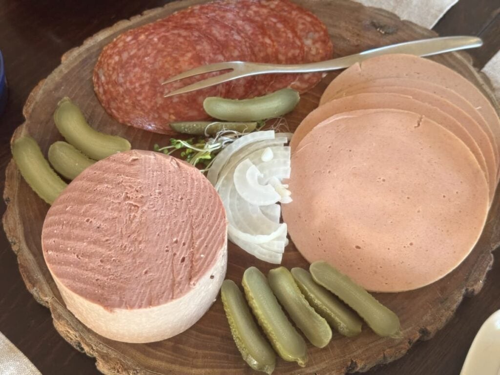 wooden board with 3 different types of cold cuts of meat with gherkins and onion slices