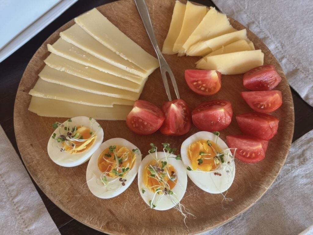 wooden board with slices of cheeses, hard boiled eggs, and tomatoes