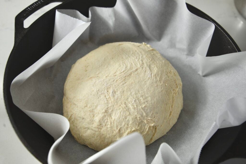 Round ball of overnight sourdough bread dough in a Dutch oven lined with parchment paper, before rising.