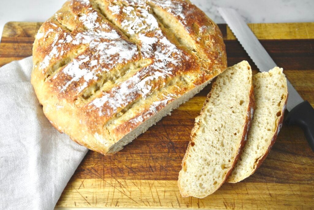 Two slices of no knead sourdough bread on a wooden cutting board, sitting next to the remaining loaf.