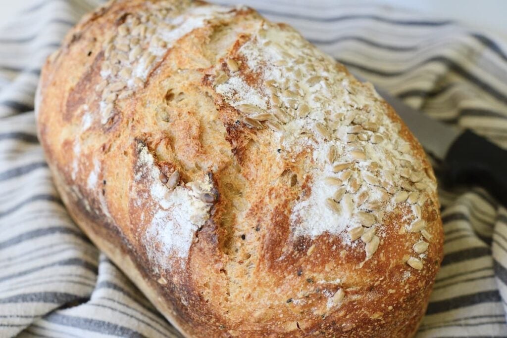 loaf of seeded sourdough bread on kitchen towel