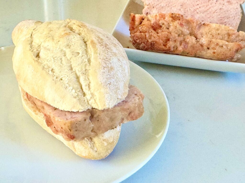 slice of Leberkaese in a crusty roll next to loaf of Leberkaese