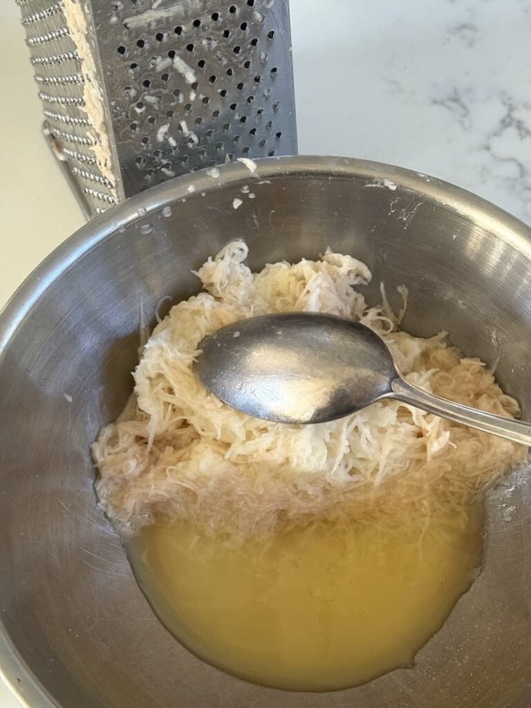 grated potatoes in bowl with spoon and water separating