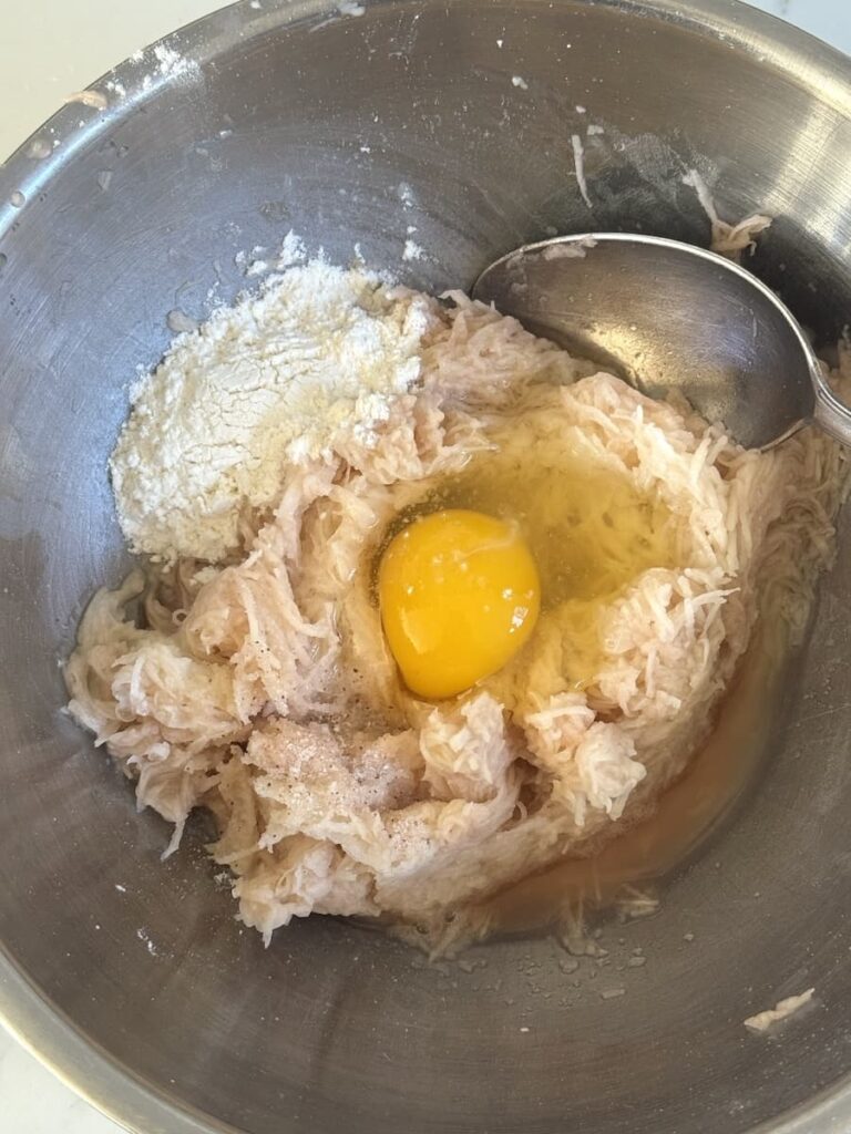 grated potatoes, egg, flour, salt in bowl with spoon