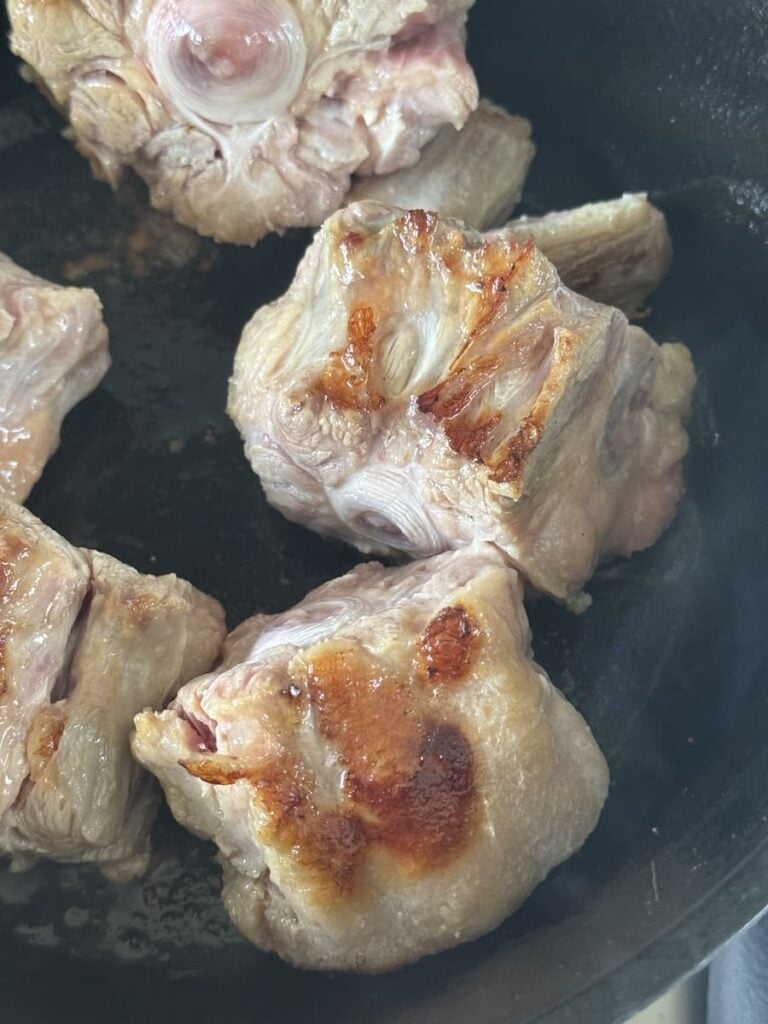 browned oxtail pieces in cast iron skillet