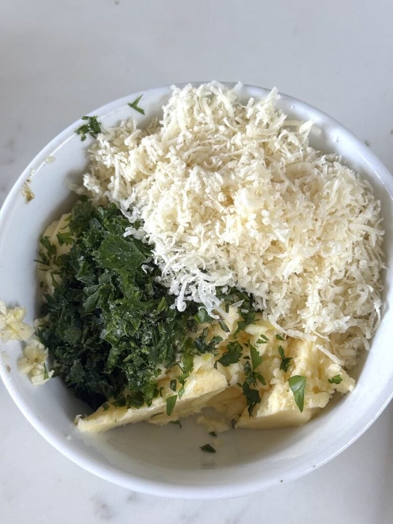 small bowl with grated cheese, butter, chopped herbs, garlic, and salt