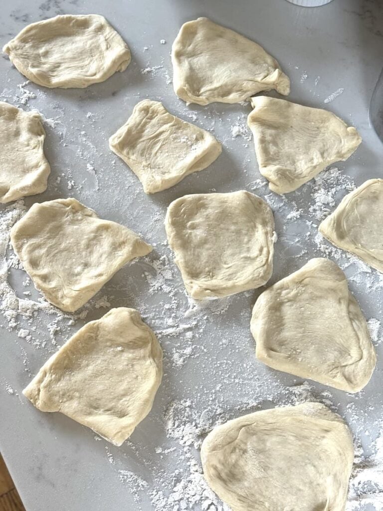 flattened dough pieces on floured kitchen counter